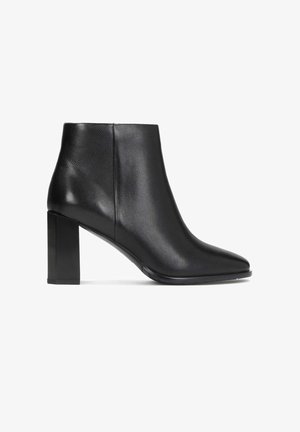 Bottine en cuir noir avec bout pointu et talon bloc épais, vue latérale sur fond blanc.