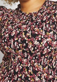 Bluse mit floralem Muster auf schwarzem Grund in den Farben Rot, Pink und Gelb. Strukturierter Stoff mit figurbetontem Design und kurzen Ärmeln.