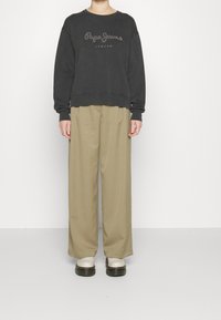 Sudadera negra de gran tamaño con el logo "Pepe Jeans London", combinada con pantalones sueltos color beige y zapatos de suela gruesa blanca. Textura de tela suave.