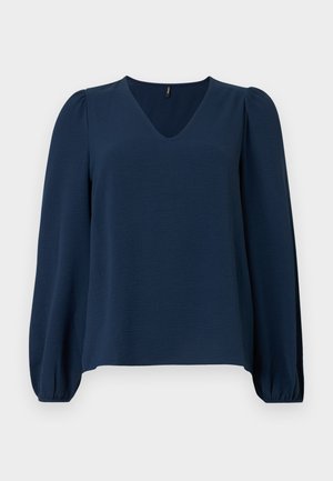 Μπλούζα σε σκούρο μπλε ναυτικό χρώμα με μακριά μανίκια, V-λαιμόκοψη, ελαφρώς φουσκωτούς ώμους και ελαστικές μανσέτες στα μανίκια σε απλό φόντο.