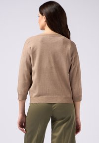 Brun, glittrande tröja med trekvartslånga ärmar och rundad halsringning, tillsammans med olivgröna byxor. Slät textur.