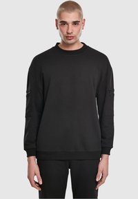 Felpa nera oversize con scollo rotondo, maniche lunghe e tasche laterali con zip. Realizzata in materiale morbido con polsini e orlo a costine.