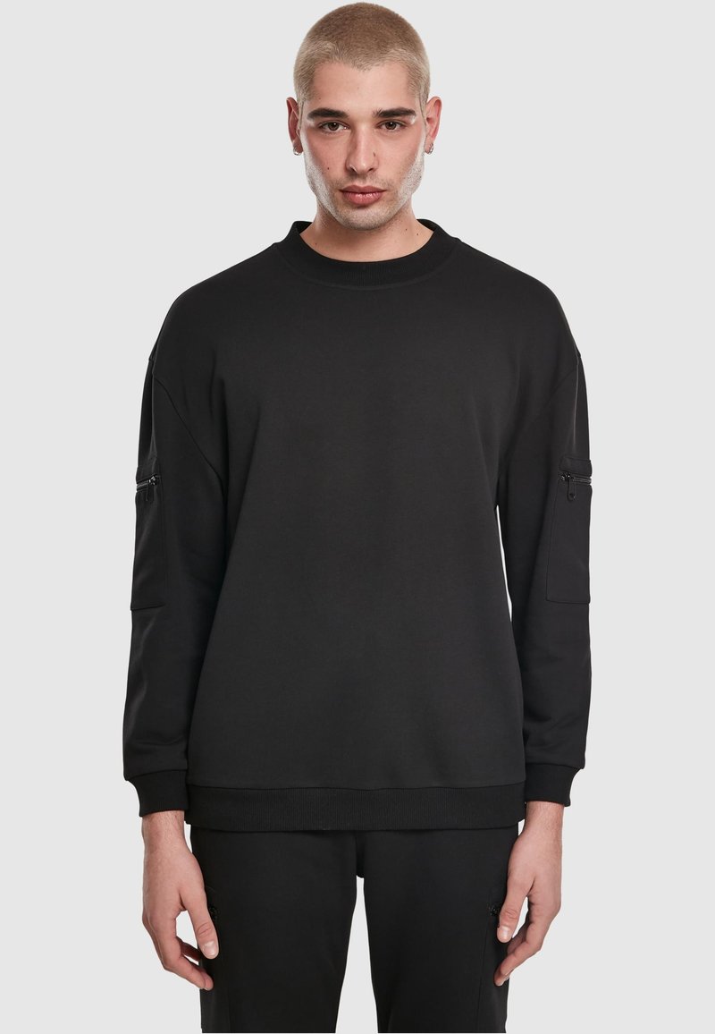 Felpa nera oversize con scollo rotondo, maniche lunghe e tasche laterali con zip. Realizzata in materiale morbido con polsini e orlo a costine.
