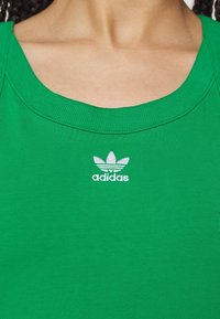 Osoba ubrana w zieloną koszulkę Adidas z białym logo Adidas umieszczonym na środku poniżej linii szyi.