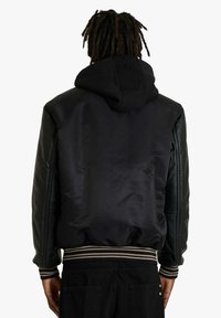 Giacca bomber nera con finitura satinata, maniche in pelle e cappuccio. Presenta polsini e orlo a coste a righe.