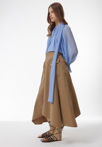 Lichtblauwe blouse met lange mouwen, gecombineerd met een knielange, bruine, A-lijn rok. Bevat twee zakken en zwarte banden sandaaltjes.