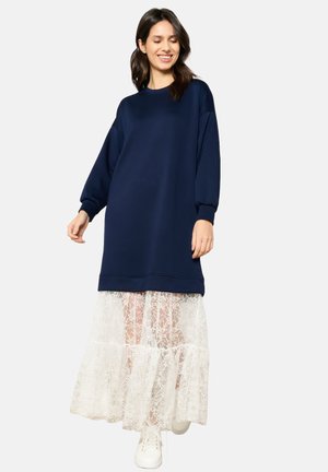 Abito nel colore blu navy con maniche lunghe, con sovrapposizione di gonna in pizzo bianco trasparente. Tessuto semplice con polsini elasticizzati e scollatura rotonda.
