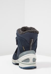 Bota azul marino con suave forro de piel de pelo gris, ante texturizado y materiales sintéticos, que cuenta con un talón reforzado y un cierre con correa ajustable.