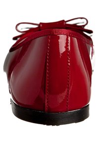 Bailarina de charol rojo con puntera redondeada y suela de goma negra. Presenta un lazo en la parte delantera. Acabado suave y brillante.