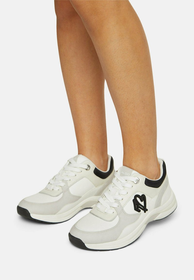 Sneakers bianchi con accenti grigi, caratterizzati da una texture liscia, forma arrotondata, dettaglio del logo nero sui lati e suole in gomma spesse.