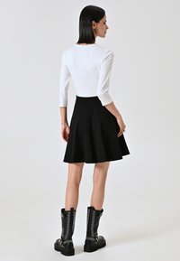 Gonna nera svasata abbinata a una maglietta bianca a maniche lunghe. Il modello indossa stivaletti combat neri con borchie. Design semplice con linee pulite.