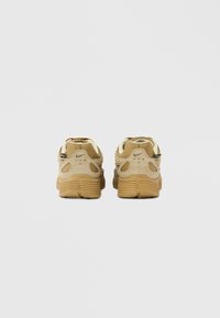 Bézs színű sportcipők texturált nubukbőr és hálós felsőrésszel, lekerekített orral, párnázott szegéllyel és hangsúlyos gumi talppal. Két sarkon lévő fül a könnyű felvételhez.
