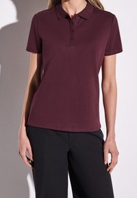 Mörkröd polo skjorta med krage och femknäpped dyna. Korta ärmar och mjukt bomullsmaterial. Kombineras med svarta byxor.