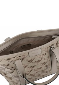 Sac fourre-tout en cuir beige avec des motifs géométriques perforés, double poignée supérieure et une poche intérieure zippée. Étiquette logo discrète visible à l'intérieur.
