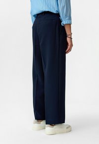 Marineblauwe wijde broek met een streepjespatroon, gemaakt van een gestureerde stof. Kenmerkt zijzakken en wordt gedragen met witte sneakers.