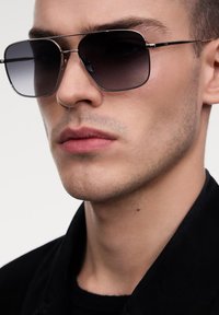 Šedé gradientové sluneční brýle s geometrickým, oversized rámem, stříbrnými kovovými akcenty a elegantním, moderním designem.