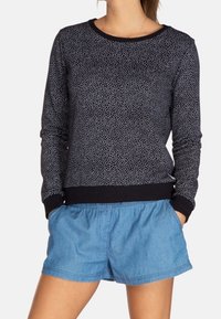 Sudadera negra con un patrón salpicado, cuello redondo y puños ajustados, combinada con pantalones cortos azules con cordón y cintura elástica.