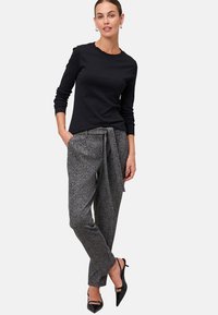 Zwarte lange mouwen top gecombineerd met hoge taille, gemusterde grijze broek met een strikceintuur. Model draagt zwarte hakken.