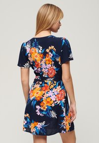 Abito floreale navy con maniche corte, caratterizzato da fiori di un vivace arancione, rosa e blu. Tessuto morbido, vita cintrata e design al ginocchio.