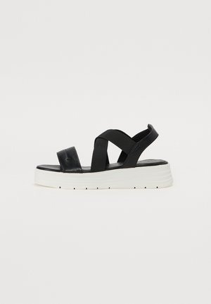 Sandalias de plataforma negras con correas elásticas, parte superior de cuero suave y suela texturizada blanca. El diseño presenta un estilo de correas cruzadas y una plantilla acolchada.