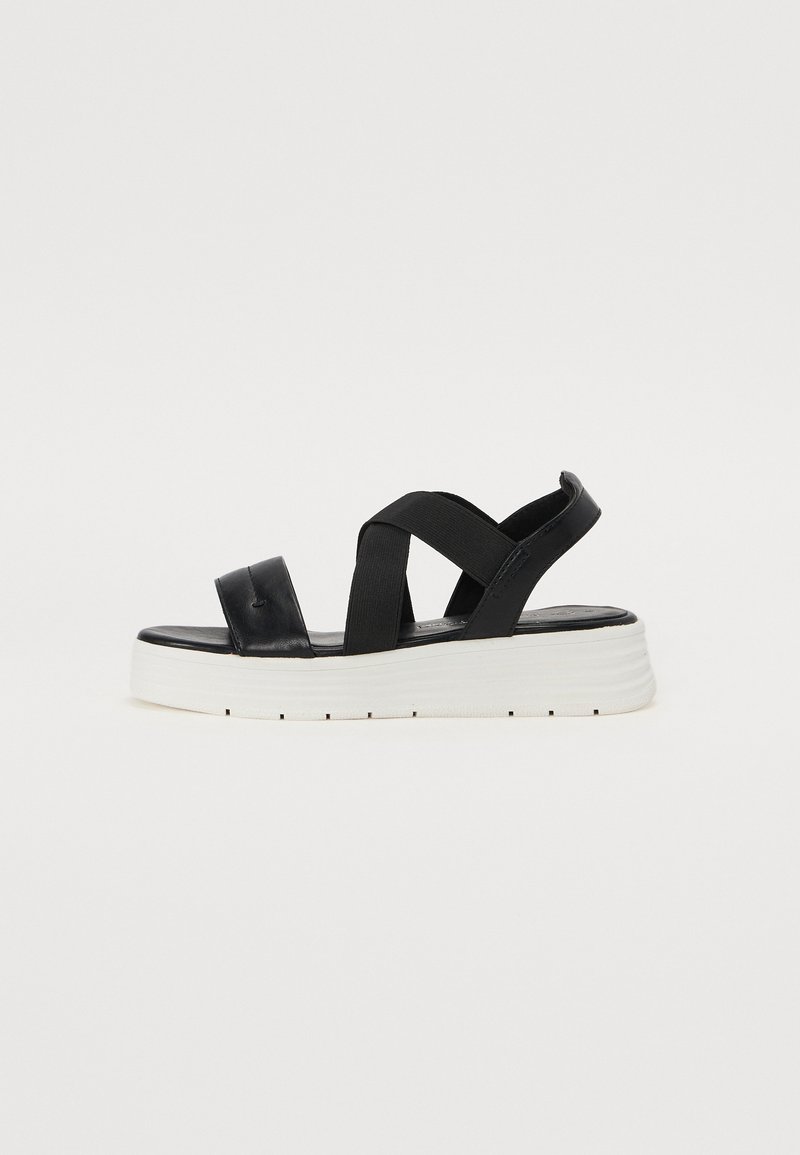 Black platform sandals with elastic straps, smooth leather upper, and a white textured sole. Design features a cross-strap style and cushioned footbed.