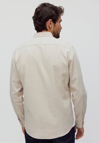Lichtbeige overhemd met lange mouwen, voorzien van een knoopsluiting voor de kraag en manchetten, met een gestructureerde stof en een gebogen zoom, gedragen met marineblauwe jeans.