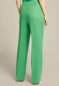 Pantaloni verdi a gamba larga realizzati in un tessuto testurizzato con elastico in vita. Presentano una vestibilità rilassata e hardware minimale, adatti per un abbigliamento casual.