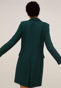 Cappotto turchese realizzato in tessuto testurizzato, caratterizzato da un colletto a risvolto, maniche lunghe, chiusura aperta e due tasche laterali.