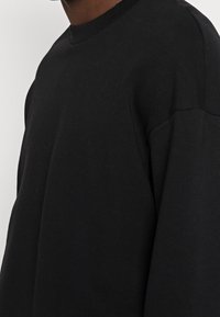 Black sweatshirt with a crew neckline, soft cotton fabric, and dropped shoulders. Features ribbed cuffs and hem with a smooth texture.