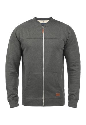 Harmaa vetoketjullinen huppari, jossa on pyöreä kaulus, kaksi etutaskua, sileä pinta ja nahkainen korostelappu helman lähellä.