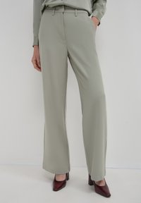 Pantalons larges gris clair avec poches latérales et une texture lisse, associés à des chaussures à talons carrés rouge foncé.