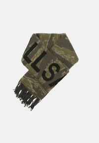Neulehuivi oliivinvihreänä, jossa on camouflage-kuvio, musta teksti ja hapsut päissä. Pehmeä, tekstuuriinen kangas.
