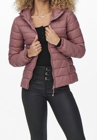 Puffer jacket in mauve with quilted design, front zipper, hood, and elastic cuffs. Paired with black high-waisted pants and a black top.