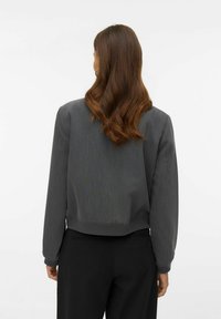 Szara krótka bluza z ściągaczami na mankietach i dole, wykonana z delikatnie fakturowanej tkaniny, o luźnym kroju, noszona na czarnych spodniach.