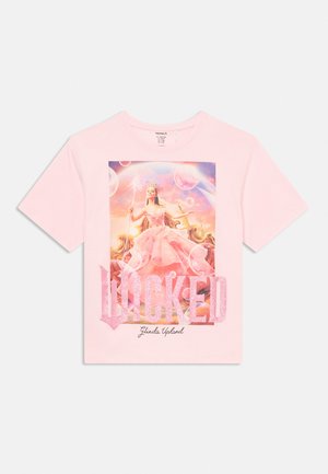 Maglietta rosa con un disegno di una principessa in un abito rosa che tiene una bacchetta scintillante, con il testo "LOCKED" e "Glinda Upland" sotto.