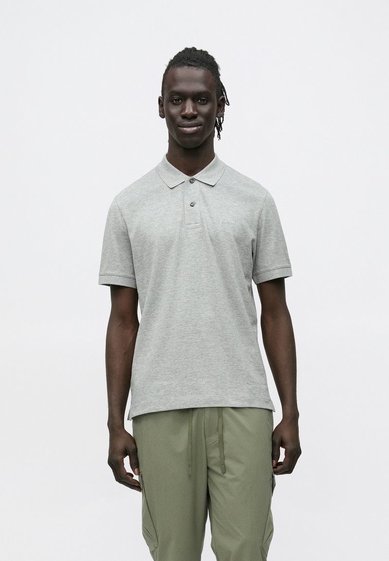 Szara bawełniana koszulka polo z kołnierzykiem, z krótkimi rękawami i rozcięciem zapinanym na dwa guziki. Dostępna w luźnym kroju, zestawiona z zielonymi spodniami typu cargo.