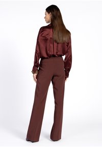 Bordeaux satijnen blouse met lange mouwen, gecombineerd met hoge taille bruine wijde broek. Snoepige textuur, minimalistisch ontwerp met subtiele details.