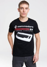 Black cotton T-shirt featuring a white retro computer graphic, red and white text reading "commodore 64," short sleeves, and a crew neck.