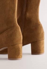 Braune Wildleder-Stiefeletten mit leichtem Absatz, seitlichem Reißverschluss und glatter Textur. Das Design umfasst eine abgerundete Spitze und minimale Nähte.