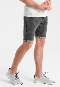 Pantalones cortos de mezclilla gris oscuro con dobladillos enrollados, combinados con zapatillas de malla blanca transpirable que presentan cordones negros y patrones texturizados.