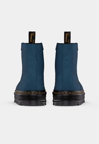 Dark blue ankle boots with textured finish, black platform sole, and yellow stitching accents. Features a pull tab at the back for easy wear.