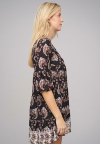 Mustahi dress dengan cetakan paisley dan bunga, lengan bergelombang, hem bertingkat, dan potongan longgar. Material tampak ringan dan bertekstur.