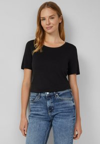 Schwarzes T-Shirt mit kurzen Ärmeln und Rundhalsausschnitt, aus weichem Stoff gefertigt, kombiniert mit blauen Jeans im klassischen Schnitt und subtilen Waschungen.