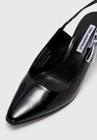 Chaussure à talons hauts en cuir verni noir avec un design à bout pointu et bride arrière. Présente une semelle intérieure de marque et une finition lisse.