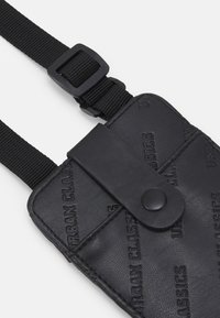Black faux leather phone pouch with embossed "URBAN CLASSICS" logo, secured by a snap button, featuring a black adjustable strap.