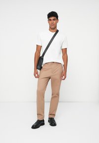 Beige bukser, hvit T-skjorte og svarte sko, med en svart skulderveske. Glatt stoff; klassisk rett ben-design. Minimalistisk stil.