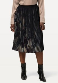 Zwarte plissé midi-rok met een patroonontwerp, voorzien van een brede elastische tailleband en een vloeiende textuur, gecombineerd met elegante zwarte enkelboots.
