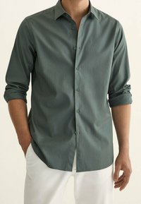 Langdurige blouse met lange mouwen in gedempt groen, gemaakt van een soepele stof. Heeft een gespreide kraag, knoopsluiting aan de voorkant en opgerolde manchetten.