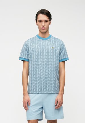 Camiseta de color azul claro con estampado, de manga corta, con cuello y puños acanalados, que presenta un pequeño logo de la marca en el pecho; combinada con pantalones cortos a juego.