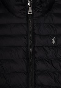 Svart puffjacka med quiltad design, heldragkedja och liten broderad logotyp på bröstet. Slätt, vattenavvisande tyg.